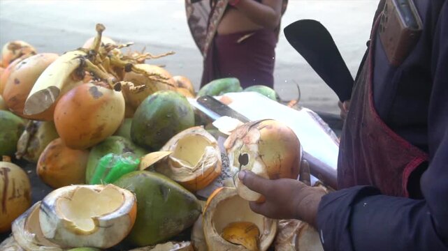 The coconut water seller is giving the coconut&rsquo;s malai (pulp) to a lady while cutting the coconut.USP