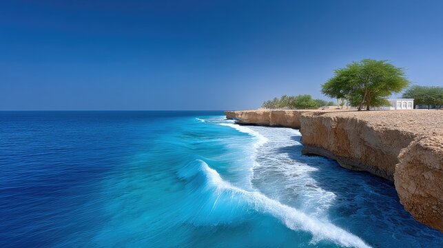 Coastal Cliffside Under Bright Daylight With Blue Ocean Waves Crashing Against Rocky Shoreline And Green Trees In The Background