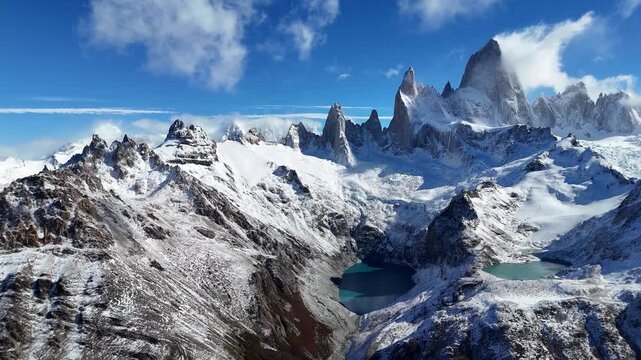 Aerial drone of Cerro Fitz Roy range in Patagonia Argentina showing snow-covered peaks, rugged ridges, and turquoise glacial lakes under clear blue sky in dramatic mountain landscape and cold terrain.