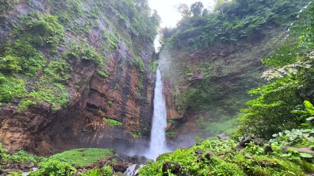 Koban Kapas Biru is a waterfall in the tropical jungles of East Java, descending from a high cliff into a lush green canyon surrounded by tropical forests with vibrant vegetation.Lumajang River. 4К