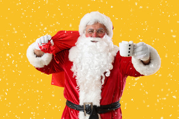 Santa Claus with Christmas bag and cup of cacao on yellow background