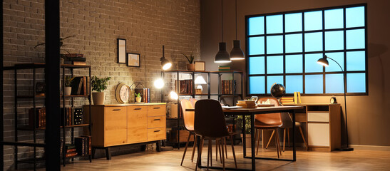 Interior of dark room with bookshelves, tables and glowing lamps at night