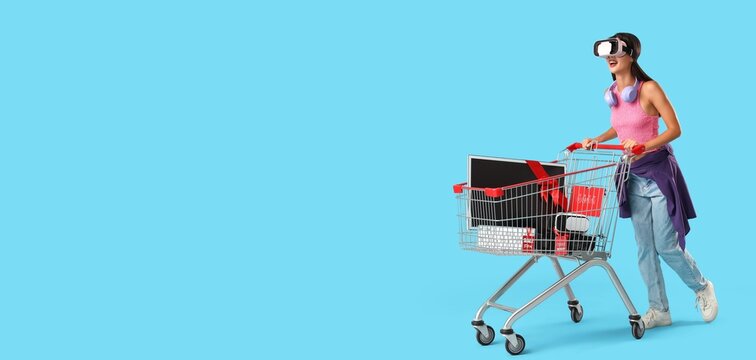 Young woman with VR glasses and devices as gifts in shopping cart on blue background with space for text. Cyber Monday