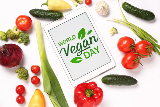 Tablet computer with text WORLD VEGAN DAY, fresh vegetables and fruits on white background