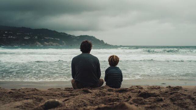 Father and son enjoy a quiet moment together on a beach, watching the waves and appreciating nature's beauty on a cloudy day