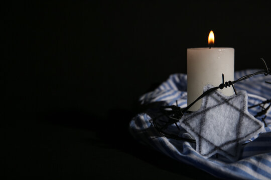 Burning candle with barbed wire, Jewish badge and prisoner uniform on dark background. International Holocaust Remembrance Day