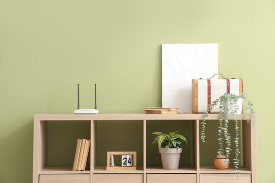 Chest of drawers with wi-fi router, plants and books near green wall