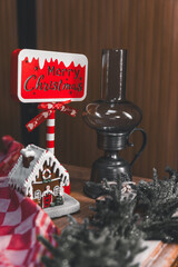 Christmas decoration with a "Merry Christmas" sign, gingerbread house and oil lamp on a wooden table with a main garland. Christmas composition on a wooden background,