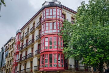 Fototapeta premium Traditional Building Corner with Red Bay Window and Balconies, Residential Facade, San Sebastian