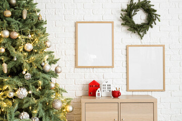 Christmas tree with festive decorations and wooden cabinet near white brick wall
