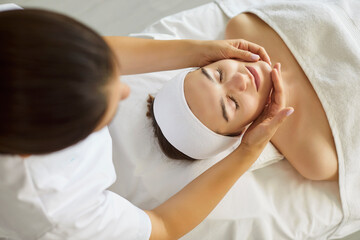 Female masseur making face relaxing massage to a young girl lying with closed eyes in beauty salon...