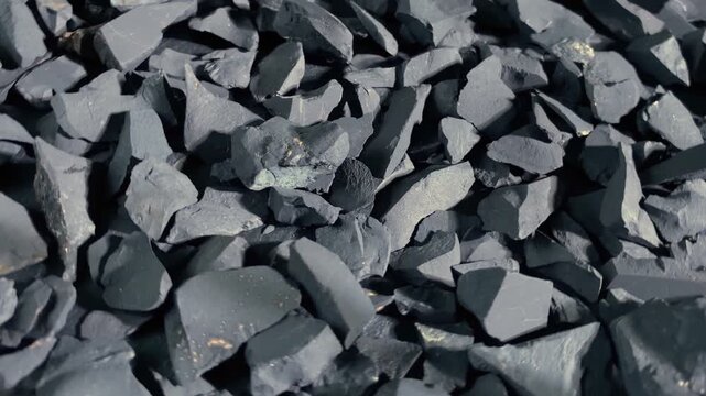 Coal or shungite stones rotating on black background. Selective focus