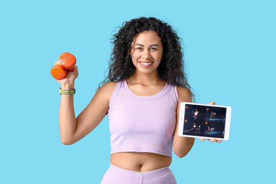 Sporty young African-American female coach with tablet computer and dumbbells on blue background. Concept of online training - Powered by Adobe