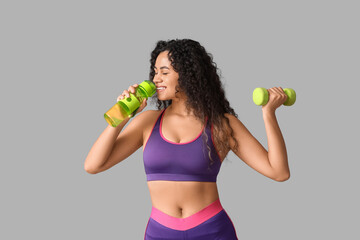 Sporty young African-American female coach with dumbbell and water bottle on white background
