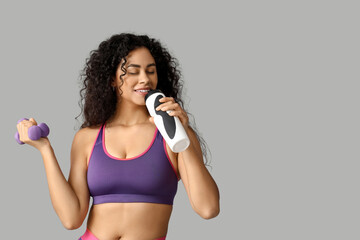 Sporty young African-American female coach with water bottle and dumbbells on white background