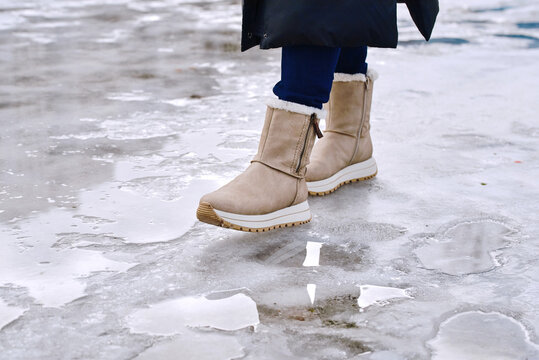 Suede boots stepping on icy frozen path with puddles during wet winter weather, risk of slipping danger while walking outdoors in hazardous cold environment. Risky winter walking on slippery path