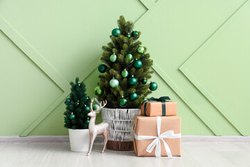 Small Christmas trees with gift boxes and decorative deer near green wall