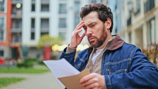 Man reads important documents outdoors, appearing concerned and stressed. Focus on financial news, unexpected problems, or critical decisions. Visuals convey worry and disappointment.