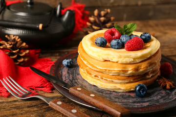 Plate of sweet pancakes with berries and pine cones on wooden background