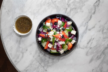 A fresh Greek salad with delicious dressing in a marble table. Includes colorful vegetables and olives