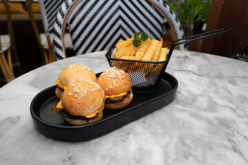 Mini burgers and french fries are a classic meal. The mini burgers are arranged in a row next to a serving of golden french fries. These delicious and tasty food sit on a stylish dark tray