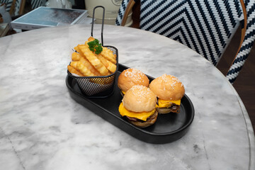 Delicious mini burgers with fries on a table. The image shows mini burgers with cheese and fries on a plate 