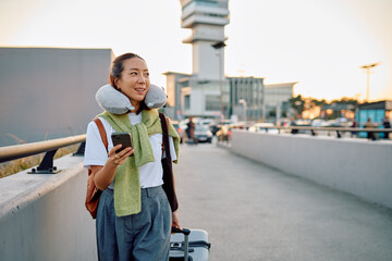 Young Asian woman arriving at airport, pulling luggage, wearing a neck pillow, smiling and checking...