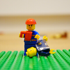 Fototapeta premium Lego construction worker confronts fallen police officer on a green baseplate
