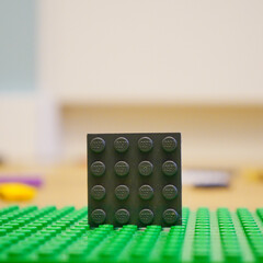 Obraz premium Black Lego brick standing on a green baseplate with a blurred background