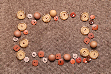 Frame made of different buttons on brown fabric background