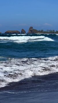 The sea in Jember, East Java. Indonesia. Watu Ulo beach with dark sand, mountains and coral rocks towering above the beach. The raging blue Indian ocean on a sunny day. 4К