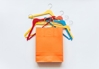 Colorful shopping bag rests on a white surface surrounded by vibrant clothes hangers, creating a cheerful and inviting retail scene.