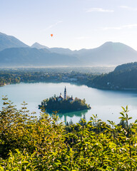 Island Church on Lake Bled with Hot Air Balloon over Mountains and Bushes in Foreground