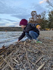 A young boy exploring the rocky shore of a serene mountain lake on a sunny autumn day.

