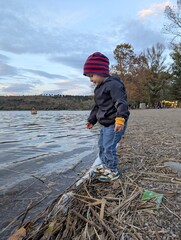 A two-year-old boy playing peacefully on the pebbled shore of a clear mountain lake, autumn sunshine.

