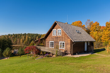 Obraz premium Rustic Wooden House Surrounded by Vibrant Autumn Forest and Sunny Landscape