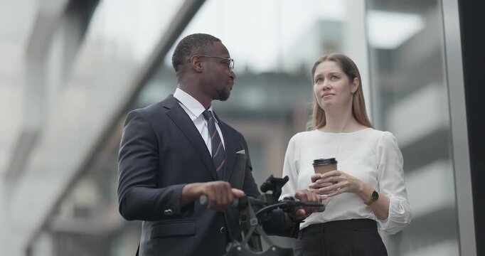 Two business colleagues commute through the city on an electric scooter, moving between sleek glass buildings toward the office and showcasing a modern, eco friendly work culture.
