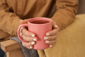 Young woman with cup of tea on sofa at home, closeup