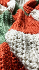 Handmade knitted blanket in orange, cream, and green colors with thick textured stitches. Cozy soft wool fabric close-up for crochet, knitting, home decor, and DIY craft inspiration.