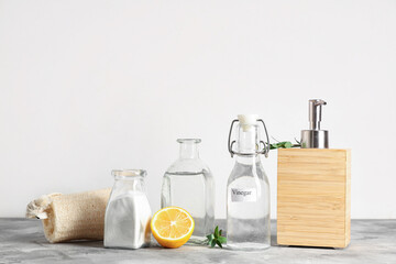 Bottles of vinegar with baking soda, lemon and soap on grey grunge table against white background