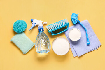 Bowls of baking soda with bottle of vinegar and cleaning supplies on yellow background