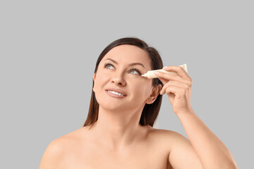Fototapeta premium Beautiful adult woman with tube of under-eye cream on white background