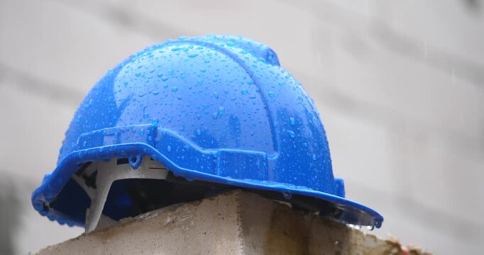 Raindrops on a safety blue helmet  placed on a pile of bricks against the background of a house under construction, construction site, construction problem concept.