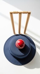 Red Cricket Ball on Blue Sun Hat, Wooden Wickets Background, White Surface, Sports Equipment Still Life