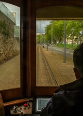 A person is driving a tram on a track, with a view of the road and trees outside the window.