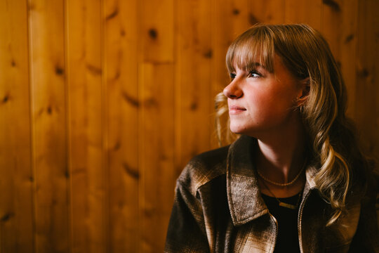 Beautiful blond young woman looks into light on wood wall