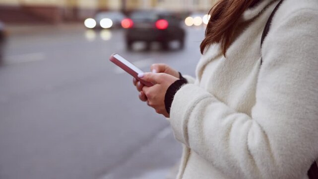 Woman using phone app to call taxi on urban street at dusk