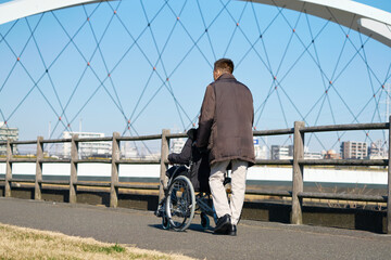 妻が乗る車椅子を押して散歩する夫　後ろ姿