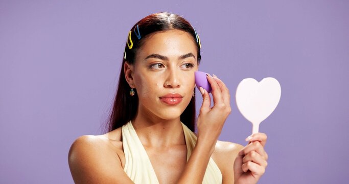 Makeup, mirror and sponge with woman in studio for cosmetics, contour and beauty maintenance. Self care, glow and blush with person on purple background for highlighter shine, foundation and gen z