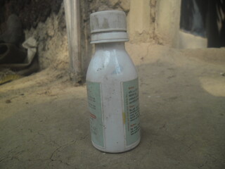 Small white plastic bottle with a cap sitting on a dusty surface